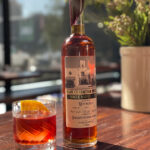 a boulevardier cocktail next to a bottle of republique's limited edition bourbon a top a wooden table in the restaurant