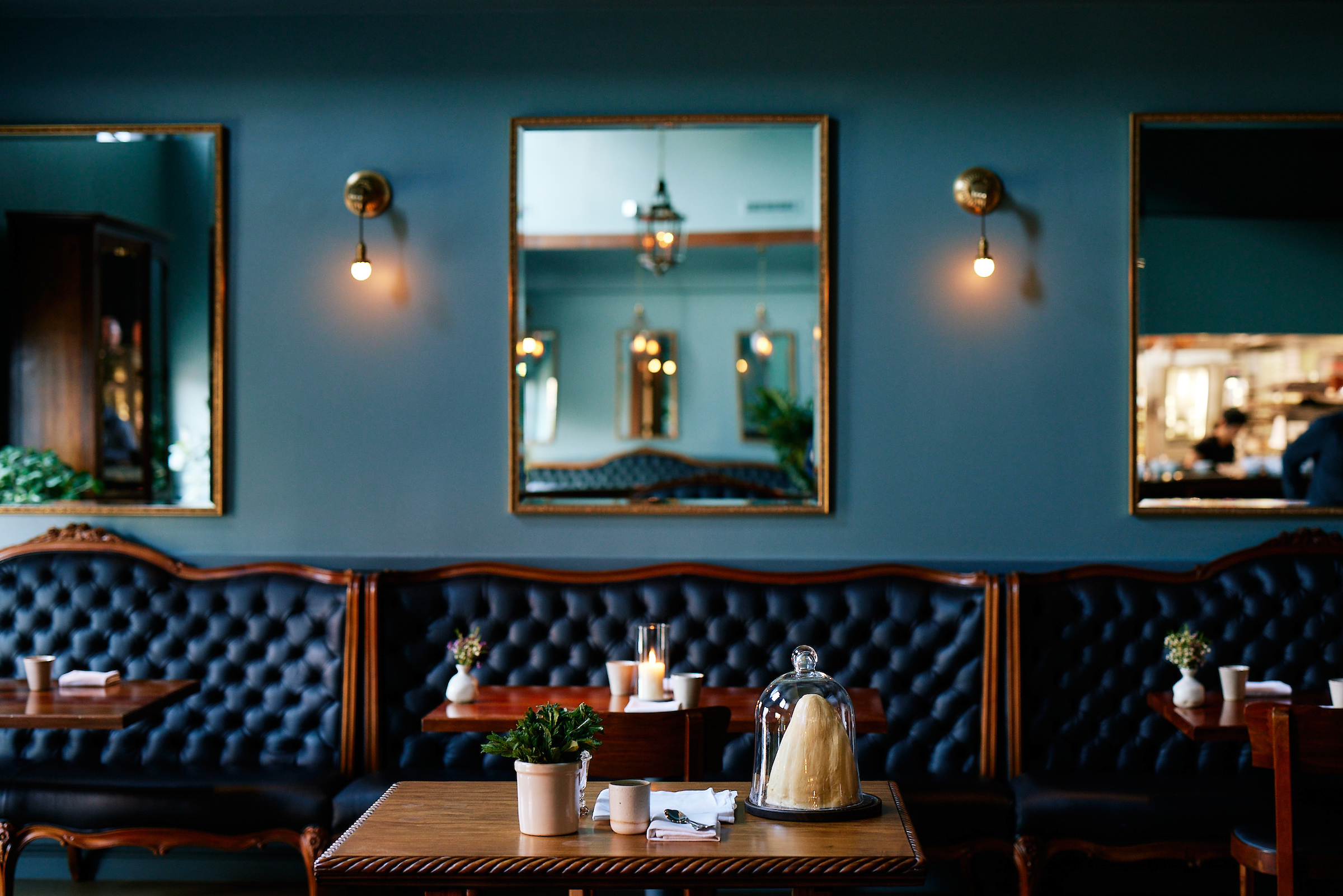 shot of wooden tables and tufted navy blue leather banquettes in the manzke dining room, which is painted in a medium blue-green hue