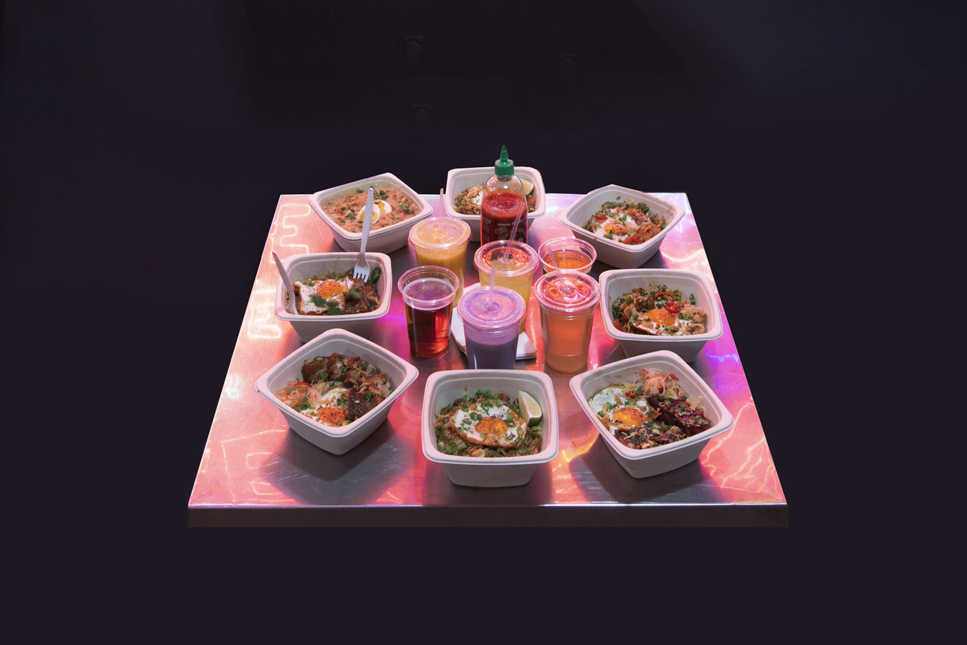 an assortment of sari sari rice bowls, beers, and juices on a stainless steel table reflecting the colors from the neon sign above