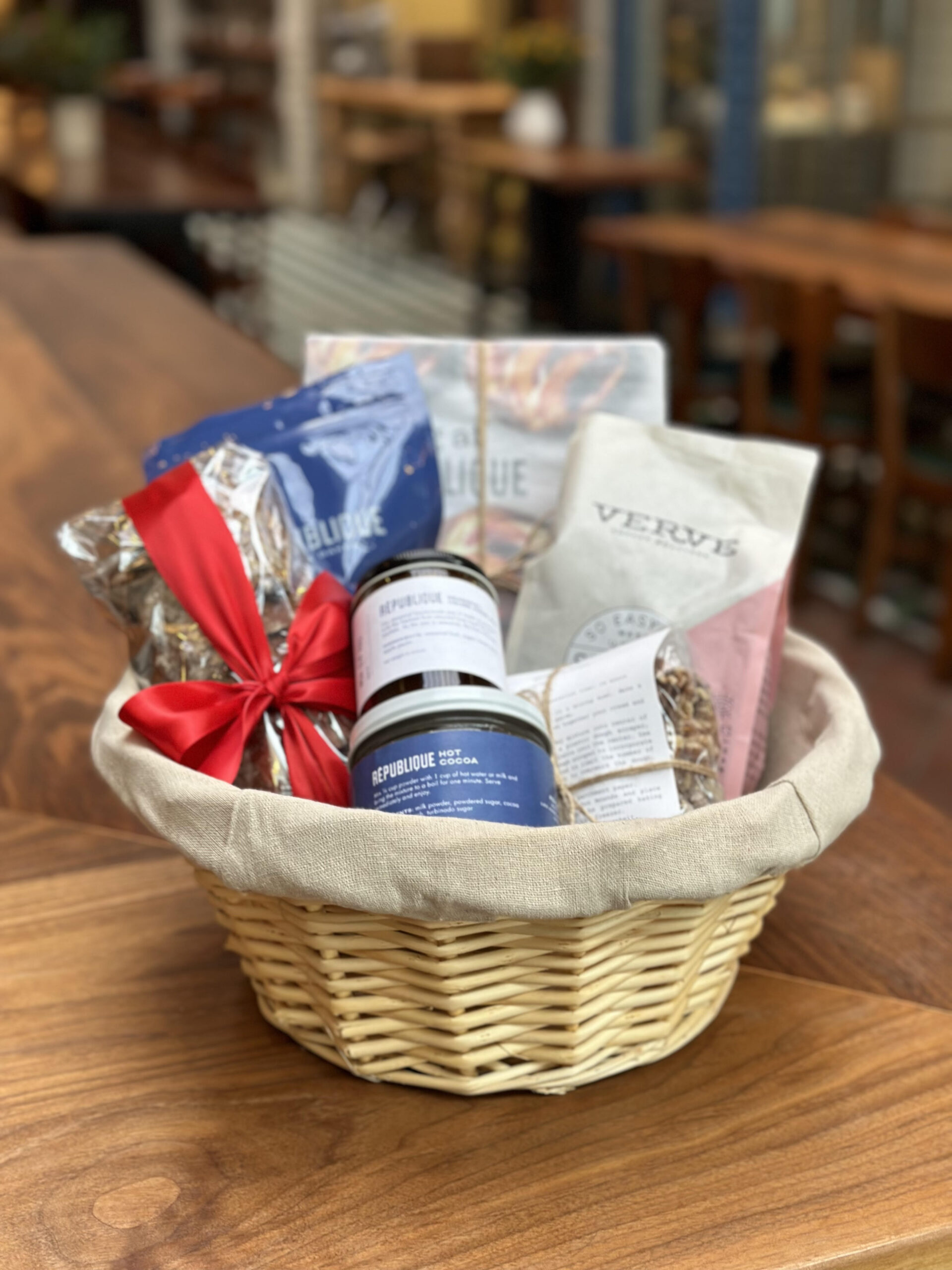 2022 holiday gift basket at republique, featuring granola, coffee, jam, cookies, cocoa mix, scone mix, and a cookbook in a round wicker basket